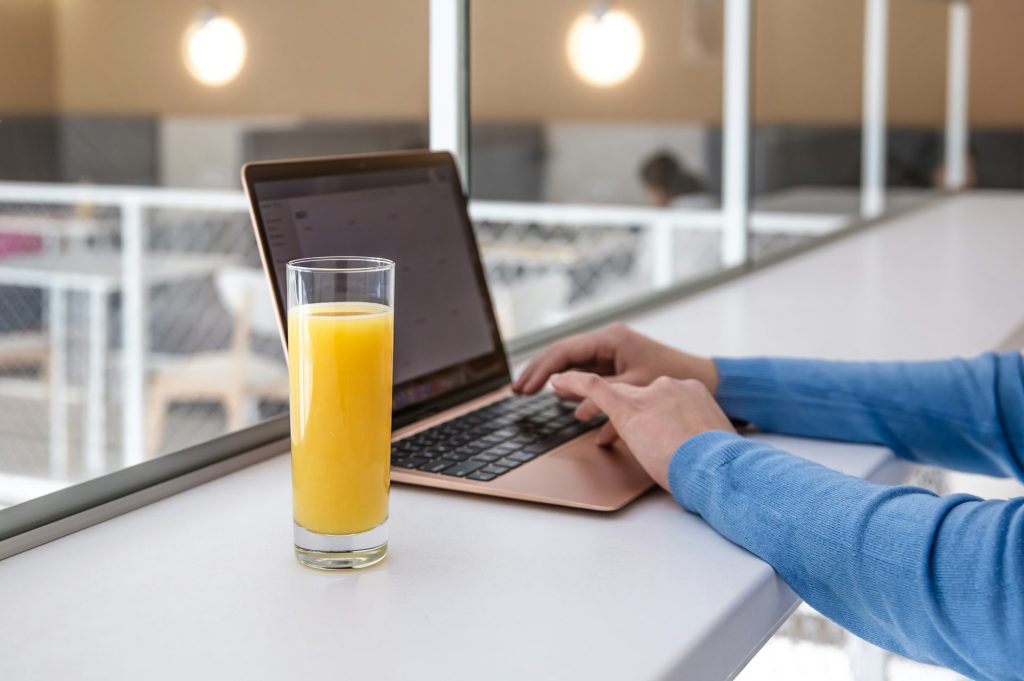 A woman works at a laptop in a cafe, drinks orange juice.