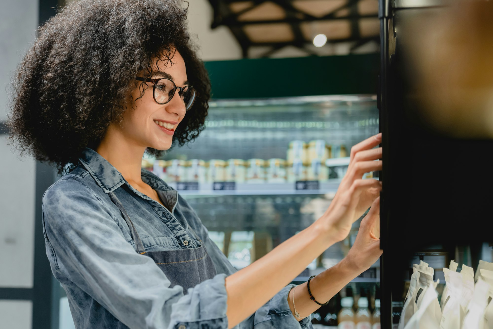 Beautiful smiling 20s female barista using vending machine in cosy coffee shop