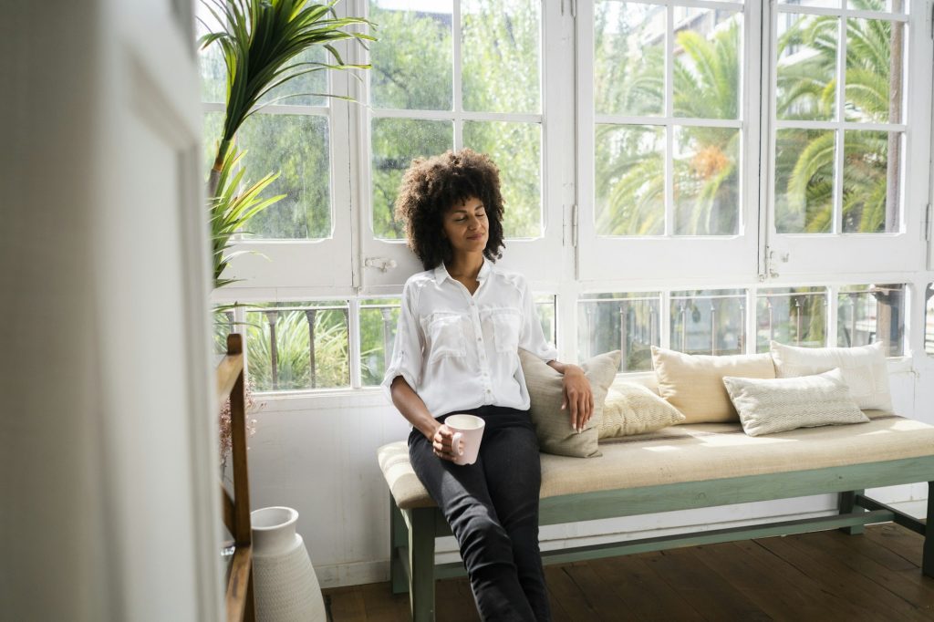 Beautiful woman relaxing on bench by the window, holding cup of coffee